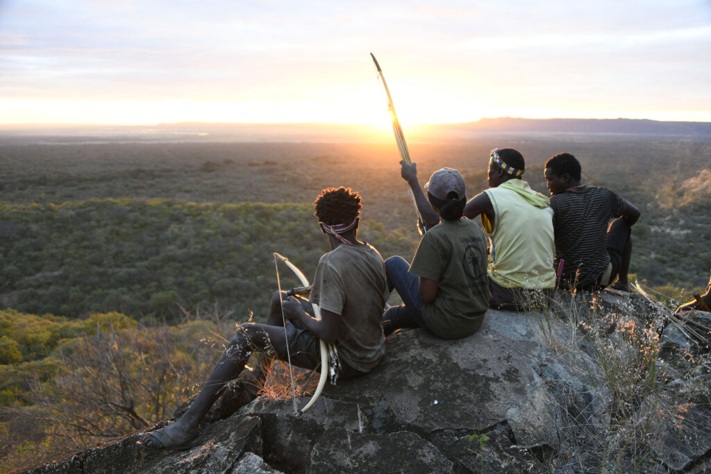 Män som sitter på en klippa med spjut i Tanzania och tittar ut över solnedgången