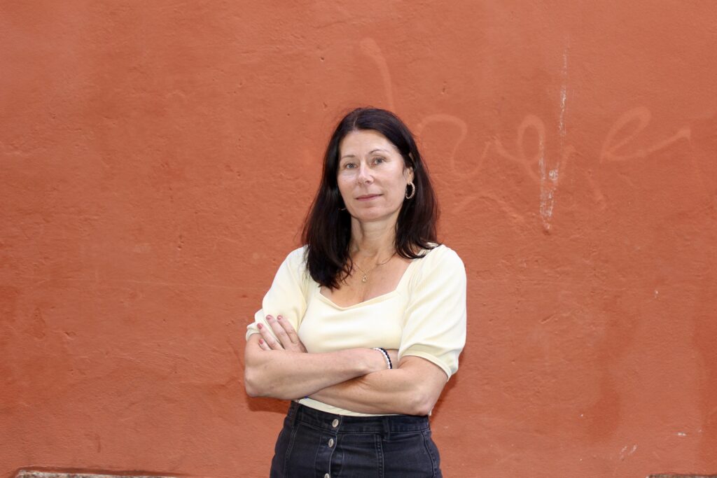 En kvinna med mörkt hår framför en röd vägg. 
