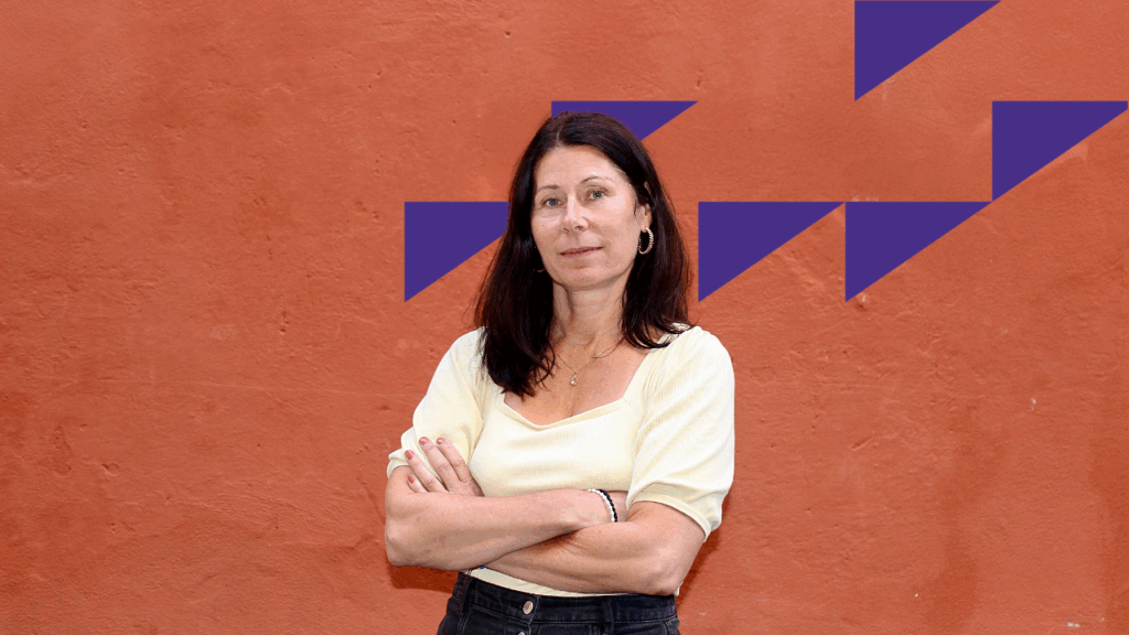 En kvinna med mörkt hår som står framför en röd vägg.