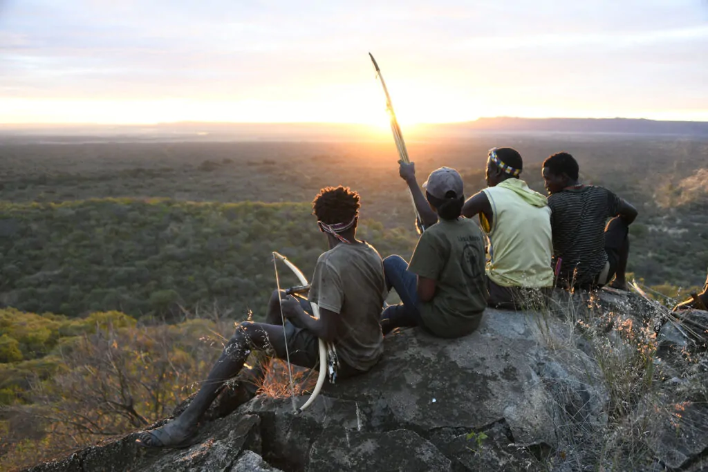 Män som sitter på en klippa med spjut i Tanzania och tittar ut över solnedgången