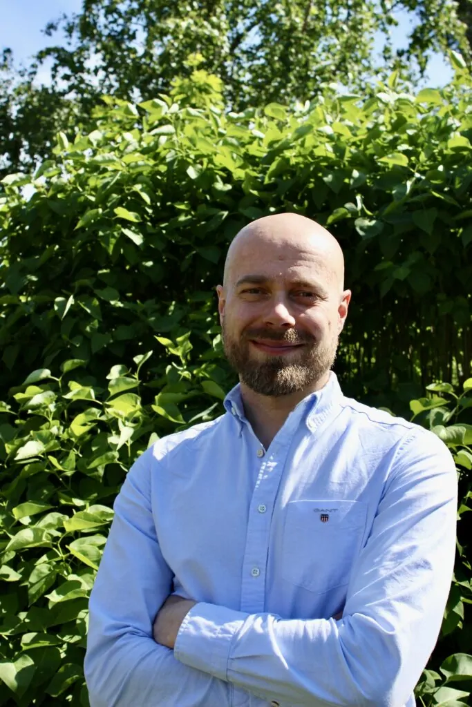 A man standing in front of a bush wearing a shirt